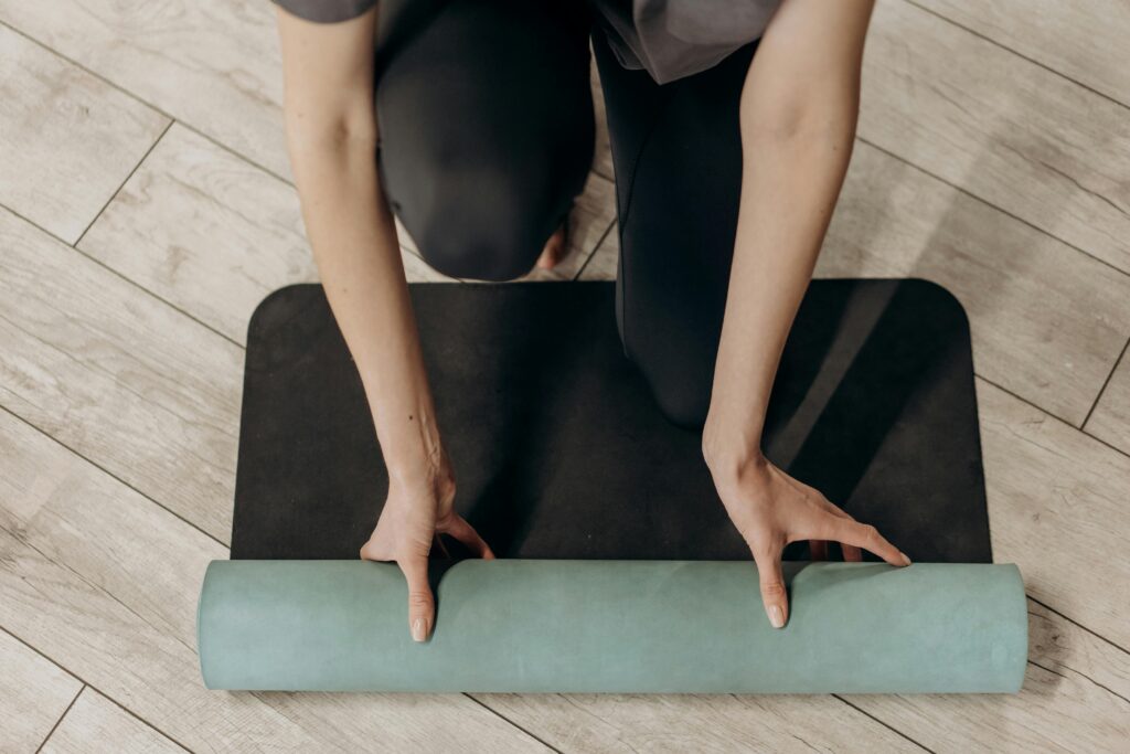 pexels-photo-6740754-6740754 Close-up of individual rolling out a yoga mat on wooden floor, ready for a home workout.